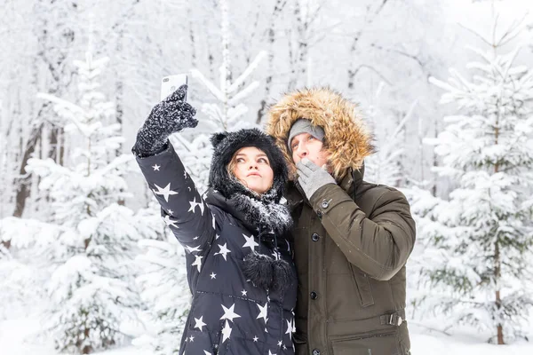 Saison, amour, technologie et concept de loisirs - couple heureux prenant selfie par smartphone sur fond d'hiver — Photo