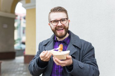 Fast food and meal concept - Young man eating take away food on the street