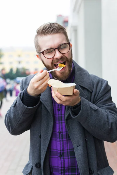 Junk food, eating and lifestyle concept - young man with meal eats on city street. — 스톡 사진