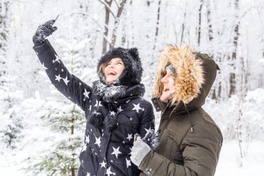 Genç romantik çiftin fotoğrafını çeken adam açık havada kar ormanlarında gülümsüyor.