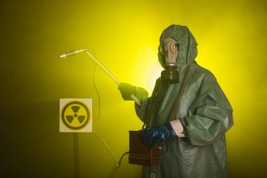 Radyasyon ve tehlike konsepti, gaz maskeli ve kimyasal giysili adam. İşçi radyoaktiviteyi ölçüyor