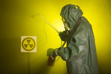 Radyasyon, kirlilik ve tehlike kavramı - koruyucu giysiler içinde bir adam ve karanlık arka planda bir gaz maskesi