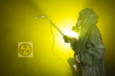 Radyasyon, kirlilik ve tehlike kavramı - koruyucu giysiler içinde bir adam ve karanlık arka planda bir gaz maskesi