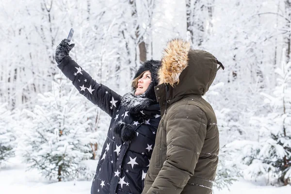 Technologies et concept de relation - Couple souriant heureux prenant un selfie dans une forêt d'hiver à l'extérieur — Photo