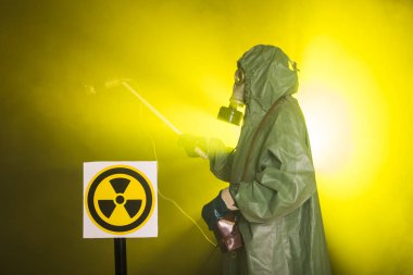 Radyasyon ve tehlike konsepti, gaz maskeli ve kimyasal giysili adam. İşçi radyoaktiviteyi ölçüyor