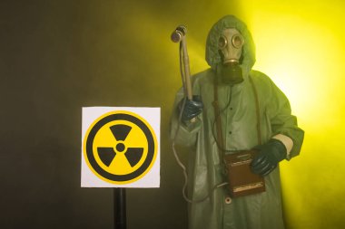 Radyasyon ve tehlike konsepti, gaz maskeli ve kimyasal giysili adam. İşçi radyoaktiviteyi ölçüyor
