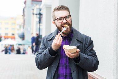 Abur cubur, yeme ve yaşam tarzı konsepti. Yemeği olan genç adam şehirde yemek yiyor..