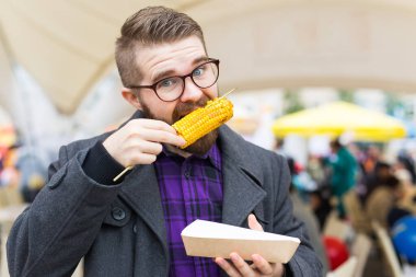 Handsome man eating roasted corn on the street.