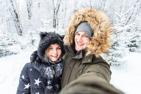Technologie i koncepcja relacji - Szczęśliwa uśmiechnięta para robi selfie w zimowym lesie na zewnątrz — Zdjęcie stockowe