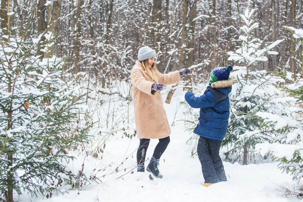 Концепция воспитания, развлечения и сезона - Счастливая мать и сын веселятся и играют со снегом в зимнем лесу — стоковое фото