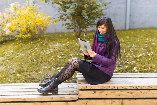 Technologies, urban and people concept - Student young woman reading an ebook or tablet in an urban autumn park