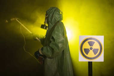 Radyasyon ve tehlike konsepti, gaz maskeli ve kimyasal giysili adam. İşçi radyoaktiviteyi ölçüyor
