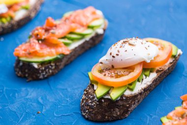 Füme somonlu sandviçler ve mavi arka planda avokado. Sağlıklı beslenme kavramı.