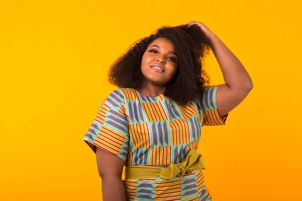 Young beautiful african american girl with an afro hairstyle. Portrait on yellow background. Girl looking at camera.