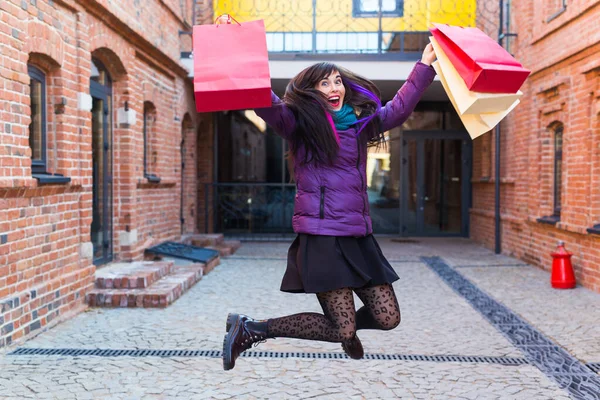 Einkaufs-, Konsum- und Verkaufskonzept - Lustige junge Frau springt mit vielen Einkaufstüten auf einer Stadtstraße — Stockfoto