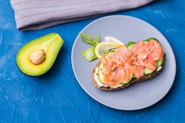 Mavi arka planda füme somon ve salatalıklı sandviç. Avokado, üst manzara. Sağlıklı beslenme kavramı.