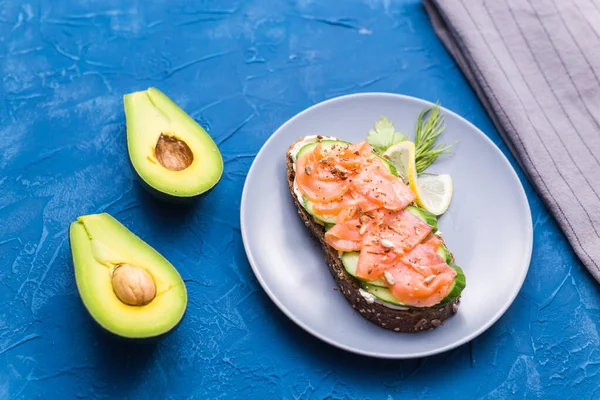 Sanduíche com salmão defumado e pepino sobre fundo azul com abacate, vista superior. Conceito para nutrição saudável . — Fotografia de Stock