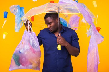 Çöp, plastik geri dönüşüm, kirlilik ve çevre kavramı sorunu - sarı arka planda çöp torbası taşıyan kafası karışmış adam