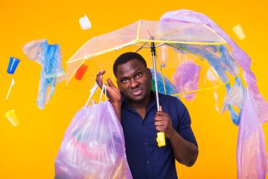 Çöp, plastik geri dönüşüm, kirlilik ve çevre kavramı sorunu - sarı arka planda çöp torbası taşıyan kafası karışmış adam