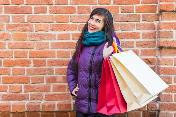 Einkaufs-, Konsum- und Verkaufskonzept - Schöne Frau mit vielen Einkaufstüten über Backsteinmauer-Hintergrund auf einer Stadtstraße — Stockfoto