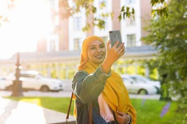 Başörtülü Müslüman kız şehrin caddesinde beklerken telefonda selfie çekiyor. — Stok fotoğraf