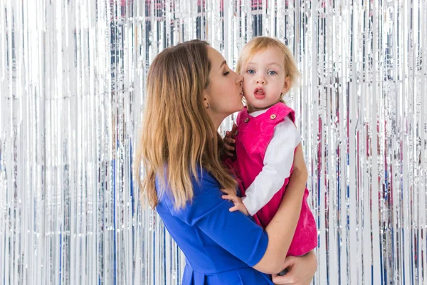 Infancia, vacaciones y concepto familiar - Madre besando a la hija sobre un fondo brillante. Primer plano — Foto de Stock