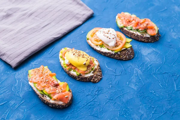 Stock image Sandwiches with smoked salmon, eggs, sauce and avocado on blue background. Concept of breakfast and healthy nutrition.