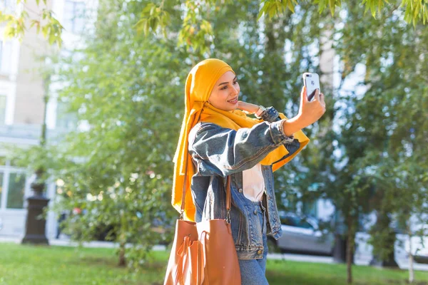 Başörtülü Müslüman kız şehrin caddesinde beklerken telefonda selfie çekiyor. — Stok fotoğraf