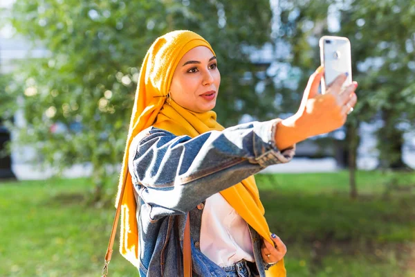 Menina muçulmana em hijab faz uma selfie no telefone de pé na rua da cidade — Fotografia de Stock