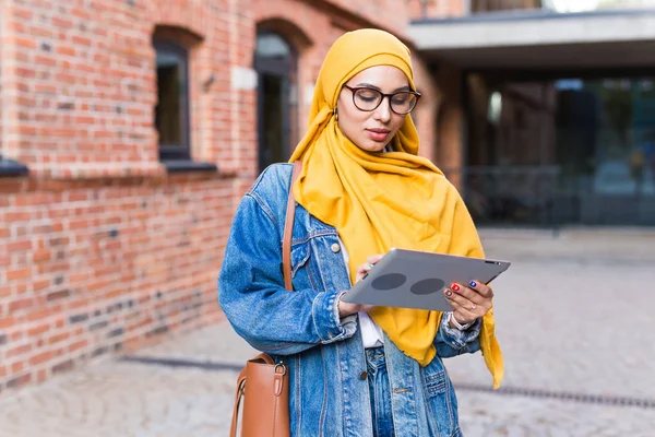 Arab woman student. Beautiful muslim female student wearing bright yellow hijab holding tablet.