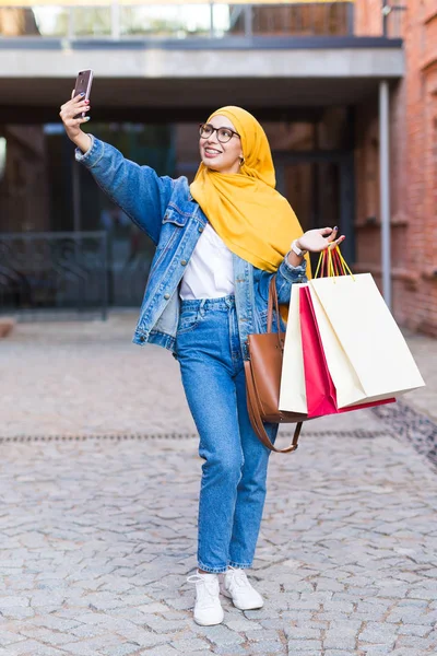 Satış, teknoloji ve satın alma konsepti - Mutlu Arap Müslüman kadın alışverişin ardından selfie çekiyor — Stok fotoğraf