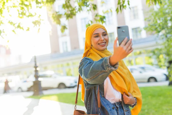 Başörtülü Müslüman kız şehrin caddesinde beklerken telefonda selfie çekiyor. — Stok fotoğraf