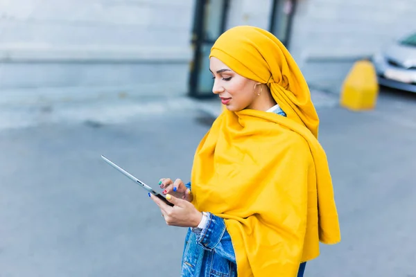 Estudante árabe. Estudante mulher muçulmana bonita vestindo hijab amarelo brilhante segurando tablet . — Fotografia de Stock