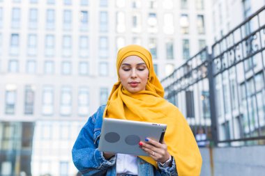 Arap kadın öğrenci. Sarı tesettürlü güzel Müslüman kız öğrenci elinde tablet tutuyor..