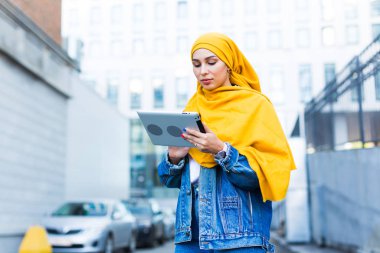 Arap kadın öğrenci. Sarı tesettürlü güzel Müslüman kız öğrenci elinde tablet tutuyor..