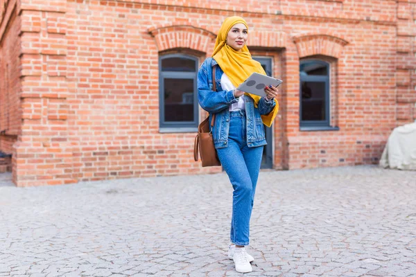 Estudante árabe. Estudante mulher muçulmana bonita vestindo hijab amarelo brilhante segurando tablet . — Fotografia de Stock