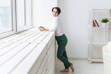 Sakin ve rahat. Evinin penceresinin yanında duran çay bardağıyla güzel genç bir kadın.