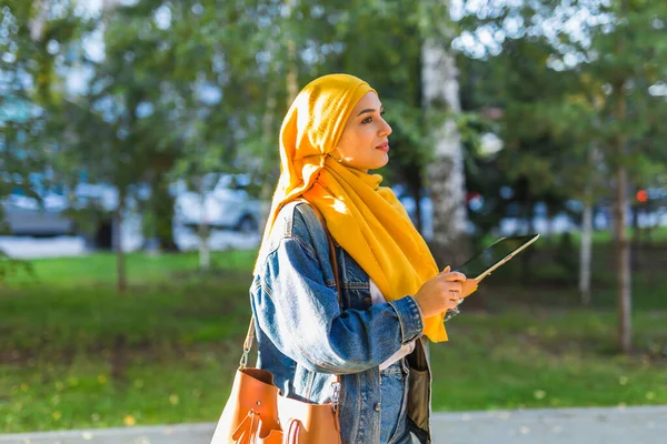 Arabisk kvinna student. Vacker muslimsk kvinnlig student i ljust gul hijab innehav tablett. — Stockfoto