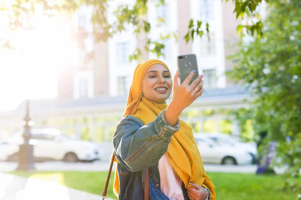 Başörtülü Müslüman kız şehrin caddesinde duran akıllı telefonda selfie çekiyor. — Stok fotoğraf