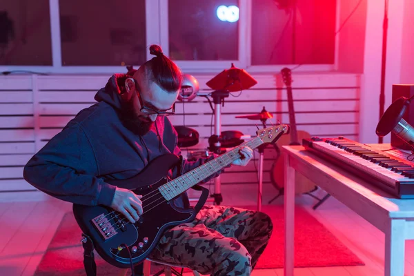 Criar música e um conceito de estúdio de gravação - Homem engraçado barbudo guitarrista gravando faixa de guitarra baixo elétrico em estúdio em casa — Fotografia de Stock