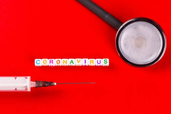 Concepto de pandemia y virus: texto del coronavirus con jeringa y fonendoscopio sobre fondo rojo. Nuevo coronavirus Covid-19 . —  Fotos de Stock