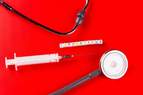 Pandemic and virus concept - Coronavirus text with syringe and phonendoscope on red background. Novel coronavirus Covid-19. — Stock Photo, Image