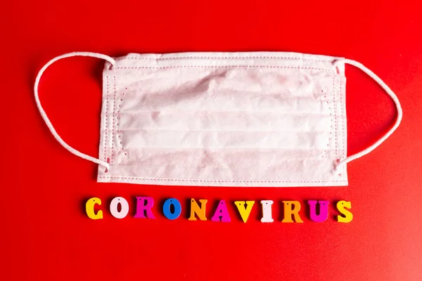 Palabra de Coronavirus hecha de letras de colores sobre fondo rojo. La inscripción en la máscara protectora médica coronavirus . —  Fotos de Stock