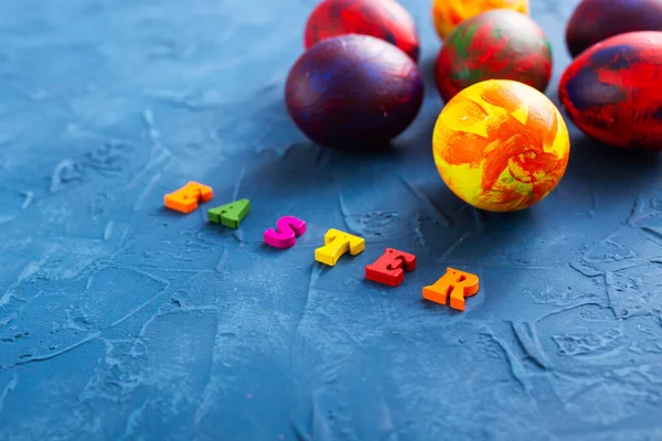 Multi-colored wooden letters making up the words happy easter and decorative colourful eggs on a blue background. Top view.