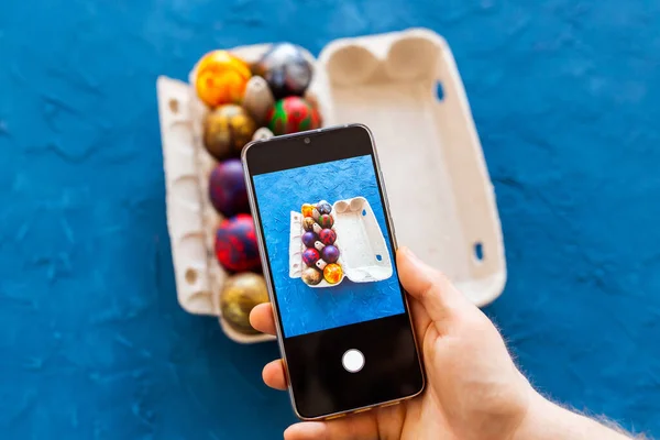 Holidays, tradition, technology and people concept - close up of man hands with smartphone taking picture of colored easter eggs.