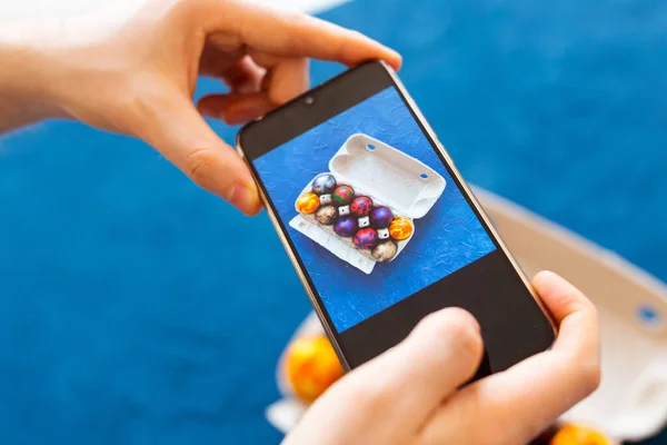 Holidays, tradition, technology and people concept - close up of man hands with smartphone taking picture of colored easter eggs.