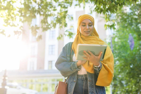Estudante árabe. Estudante mulher muçulmana bonita vestindo hijab amarelo brilhante segurando tablet . — Fotografia de Stock