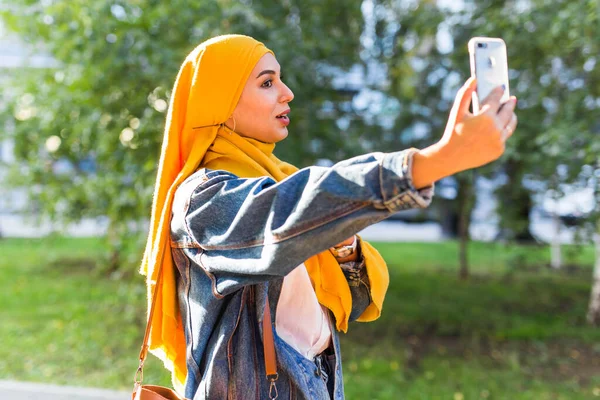 Мусульманская девушка в хиджабе делает селфи по телефону, стоя на улице города — стоковое фото