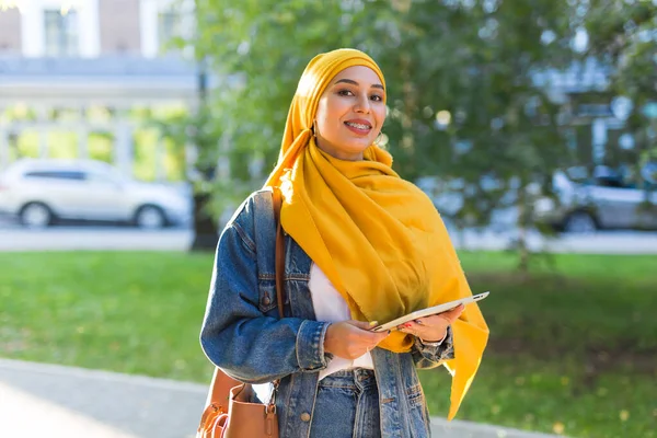Arap kadın öğrenci. Sarı tesettürlü güzel Müslüman kız öğrenci elinde tablet tutuyor.. — Stok fotoğraf