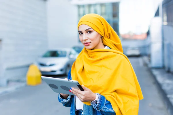 Estudante árabe. Estudante mulher muçulmana bonita vestindo hijab amarelo brilhante segurando tablet, fundo urbano — Fotografia de Stock